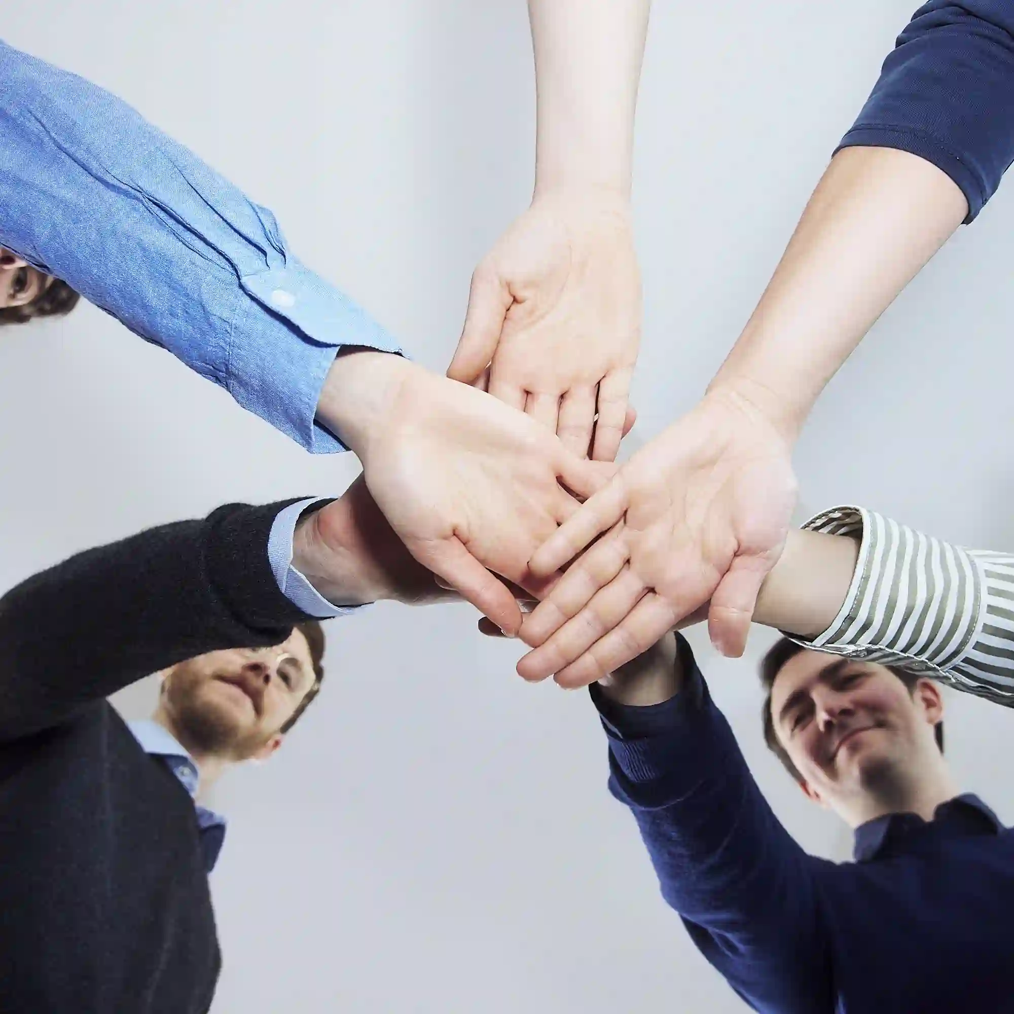 A group of diverse team members standing in a circle, reaching in with their hands stacked together in unity, viewed from below.