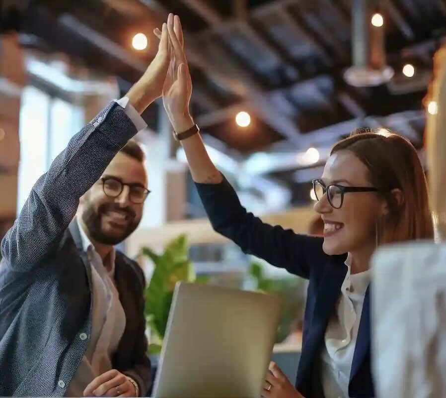 People sitting in a meeting. Two of them happily give each other a high five.