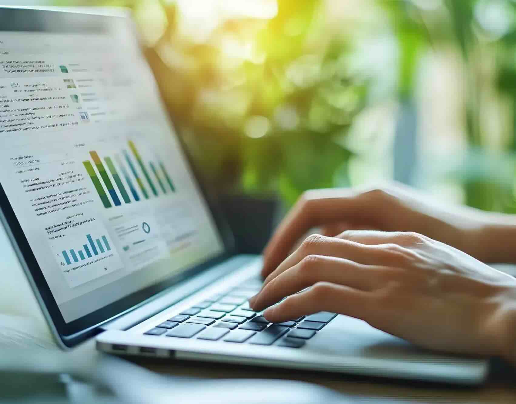 A person works on data on a laptop in an office equipped with green plants.