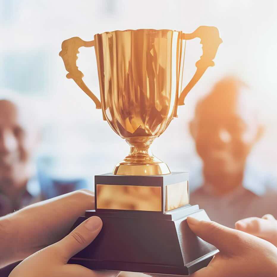 A golden trophy held by multiple hands, symbolizing achievement and teamwork, with smiling individuals in the background.