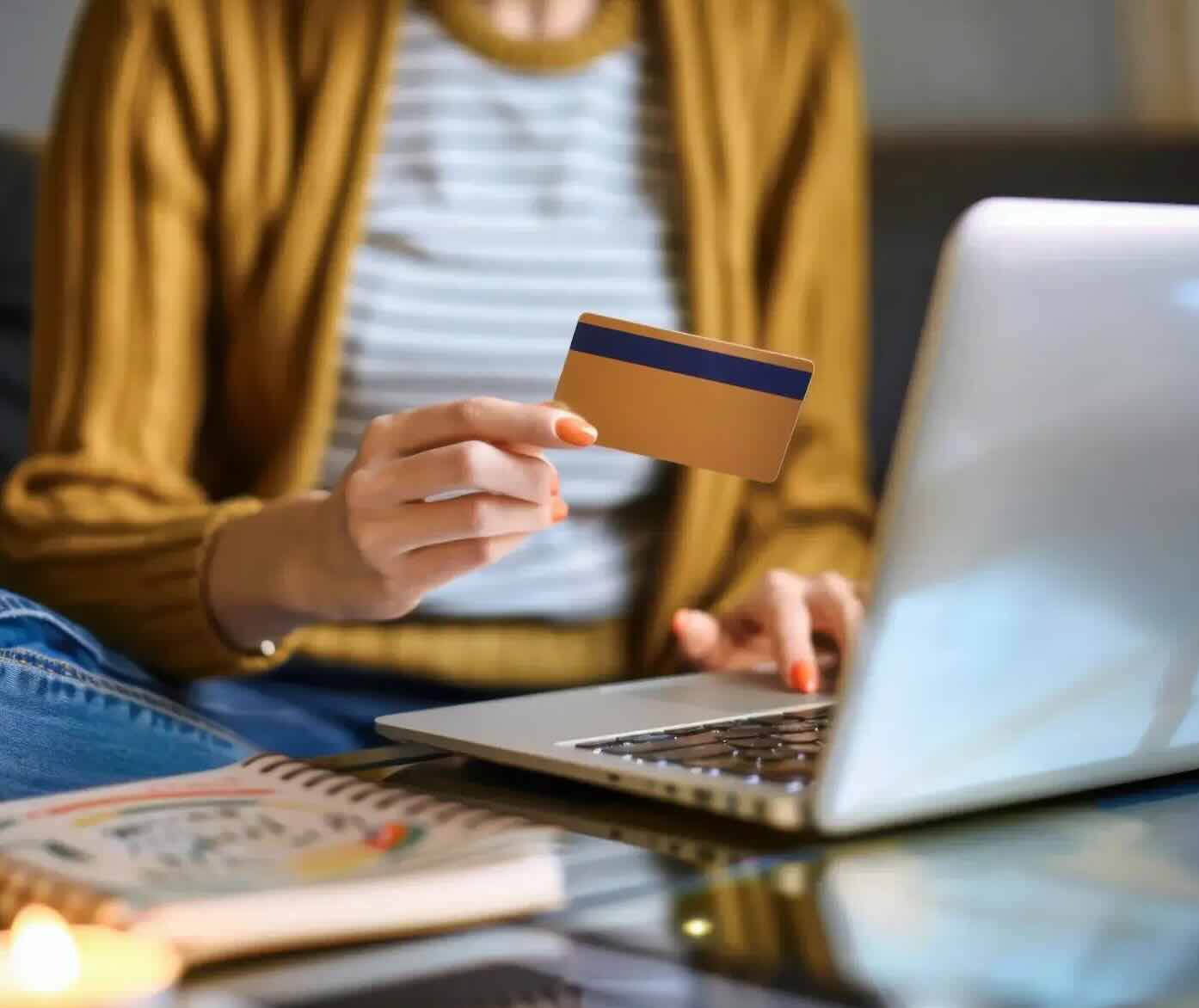 A woman sits in her living room on the couch in front of her laptop and orders something with her credit card.